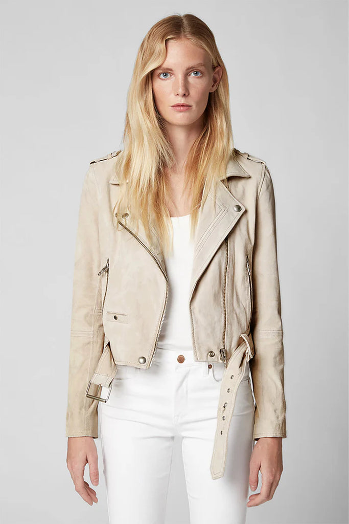 Woman wearing a beige leather jacket and white pants on a gray background