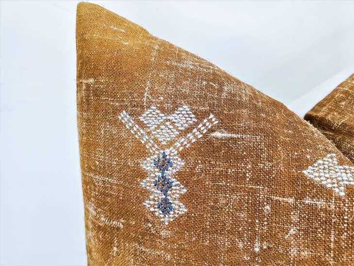 Image of the 'Moroccan Rug Design Embroidered Pillow Cover', highlighting the hand-embroidered motifs, the hand-painted color, and the handmade cotton yarn tassels.