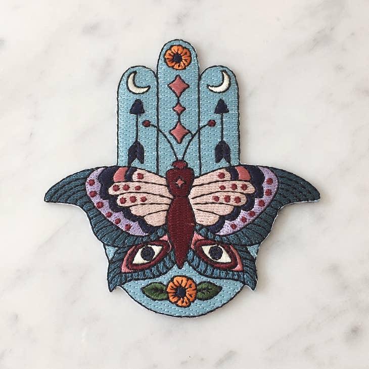Large embroidered patch displaying a Hamsa integrated with butterfly, evil eyes, crescent moons, arrows, and floral motifs in a vibrant boho color palette.