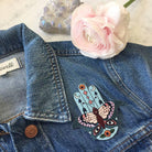 Large embroidered patch displaying a Hamsa integrated with butterfly, evil eyes, crescent moons, arrows, and floral motifs in a vibrant boho color palette.