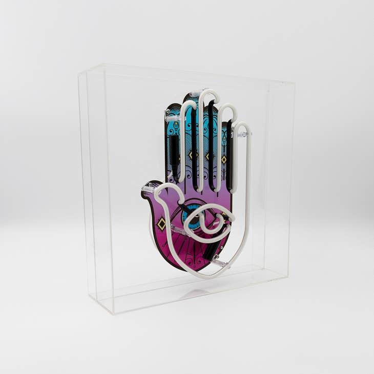 Yellow, pink, and white Neon Hamsa Hand Light encased in a glossy acrylic box with printed graphics by FORMA.