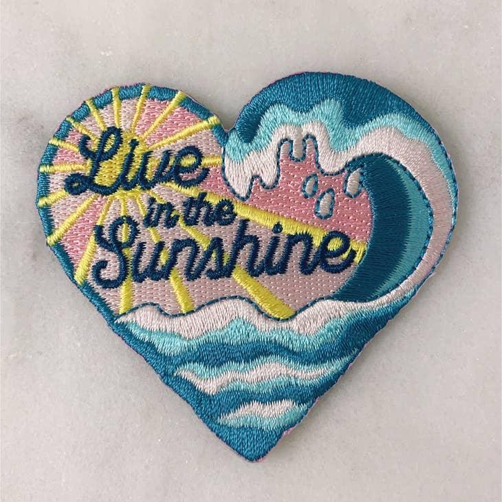 Brightly colored embroidered patch with the words "Live in The Sunshine" surrounded by radiant sun rays.