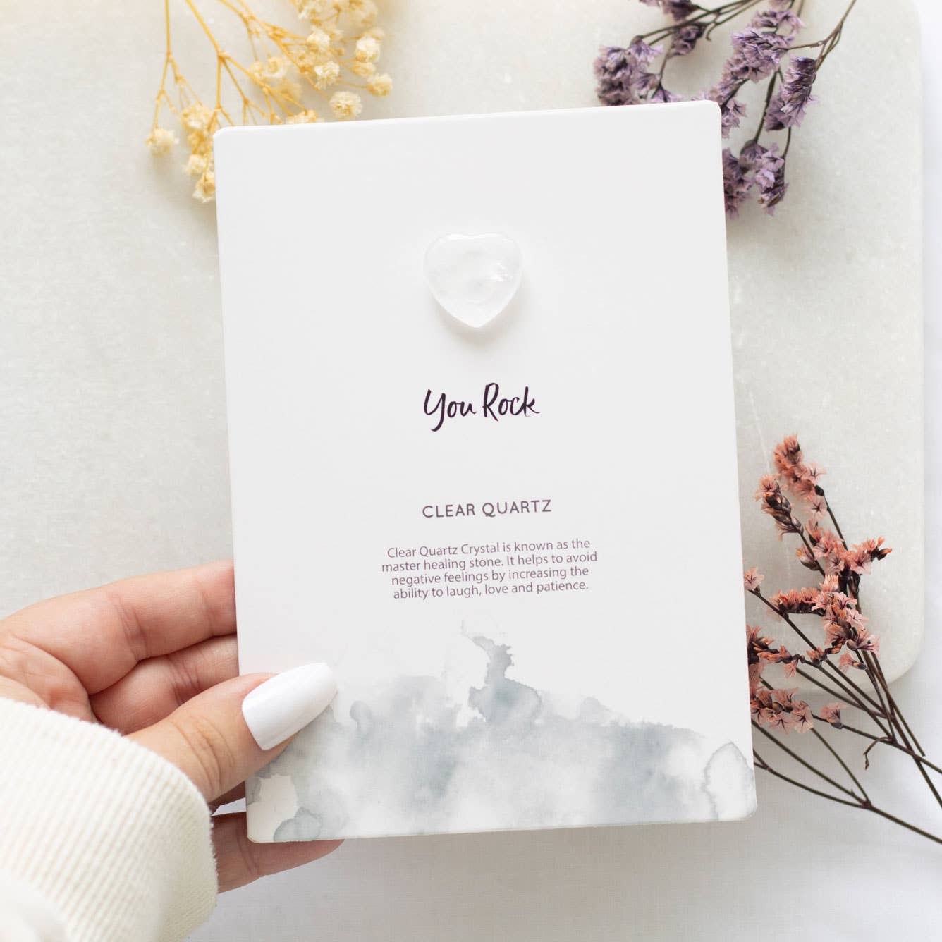 Hand holding a greeting card with a small clear quartz crystal heart and ‘You Rock’ text.
