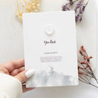 Hand holding a greeting card with a small clear quartz crystal heart and ‘You Rock’ text.