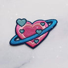 Embroidered patch showcasing a planet in the form of a heart with intricate details.