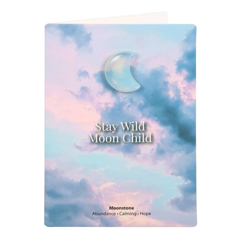 Greeting card with a moonstone crescent moon charm and ‘Stay Wild Moon Child’ text against a dreamy sky background.