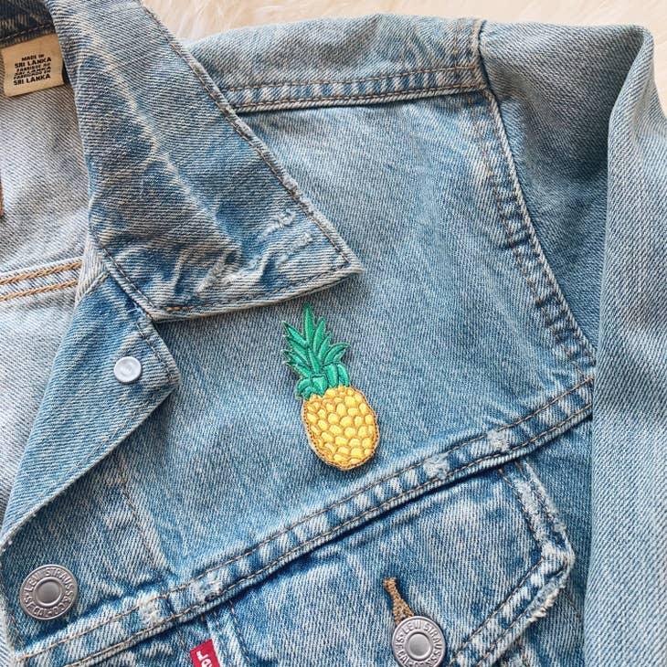 Golden embroidered pineapple patch with detailed green leaves.