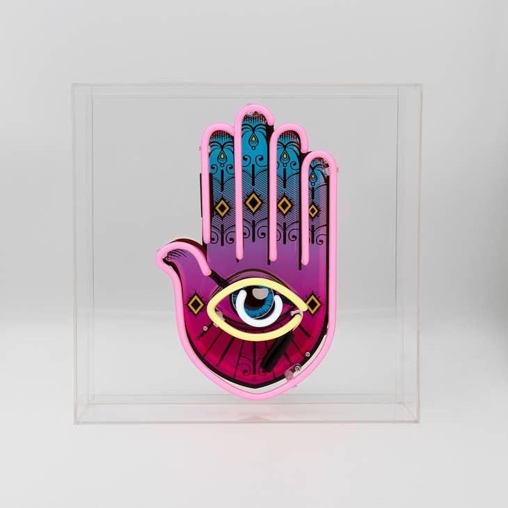 Yellow, pink, and white Neon Hamsa Hand Light encased in a glossy acrylic box with printed graphics by FORMA.