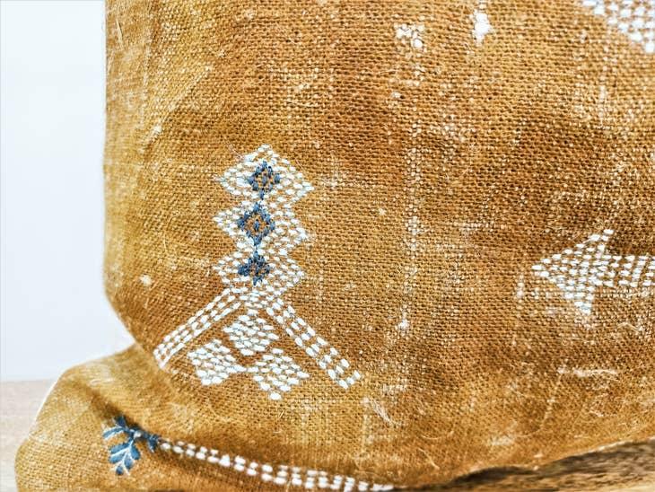 Image of the 'Moroccan Rug Design Embroidered Pillow Cover', highlighting the hand-embroidered motifs, the hand-painted color, and the handmade cotton yarn tassels.