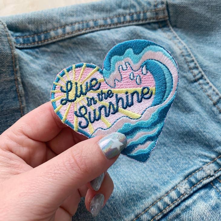 Brightly colored embroidered patch with the words "Live in The Sunshine" surrounded by radiant sun rays.