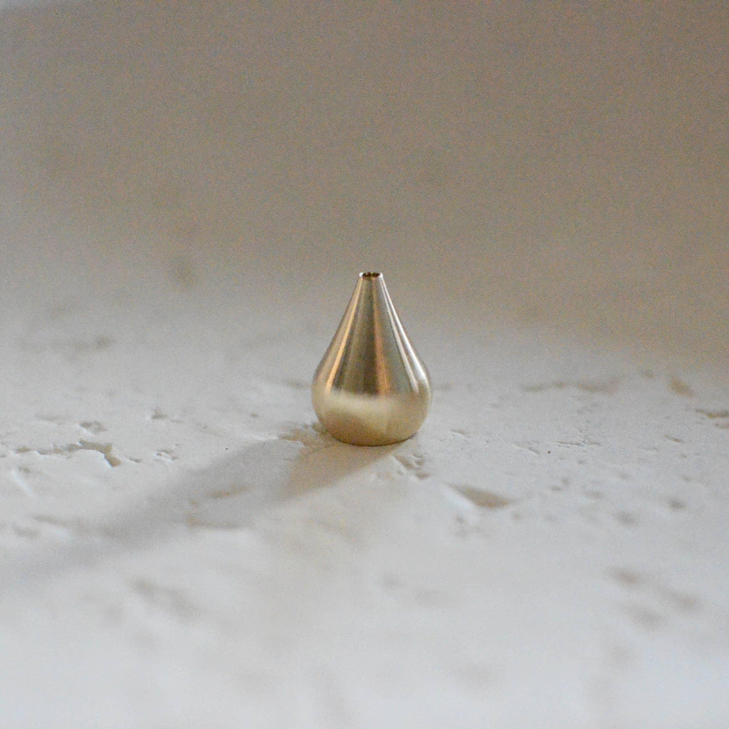 Elegant Brass Water Drop Incense Holder placed on a neutral backdrop, casting a warm glow, ideal for holding incense in style.