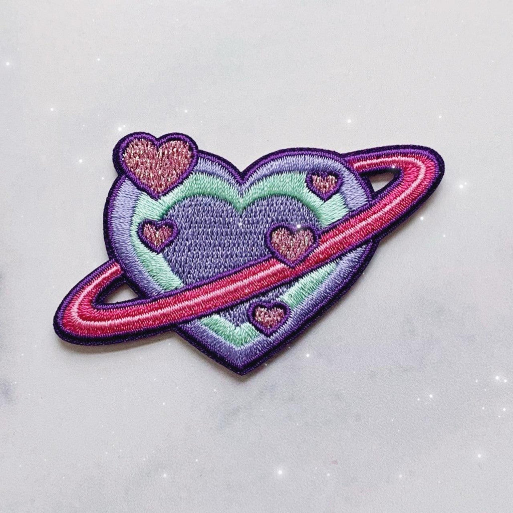 Embroidered patch showcasing a planet in the form of a heart with intricate details.