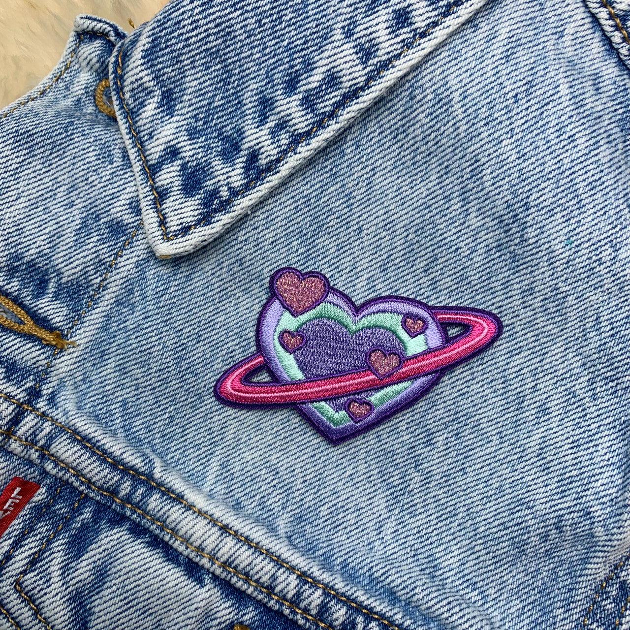 Embroidered patch showcasing a planet in the form of a heart with intricate details.